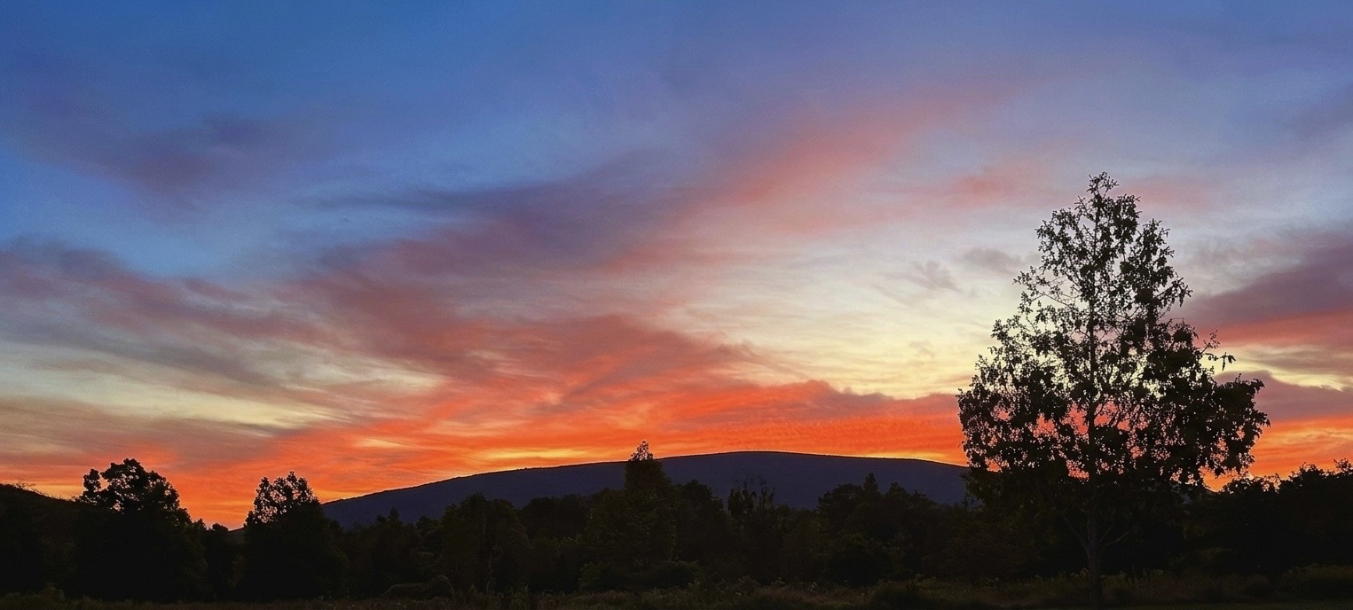 A ridge of hills stands in silhouette against a wide, burning sunset sky.