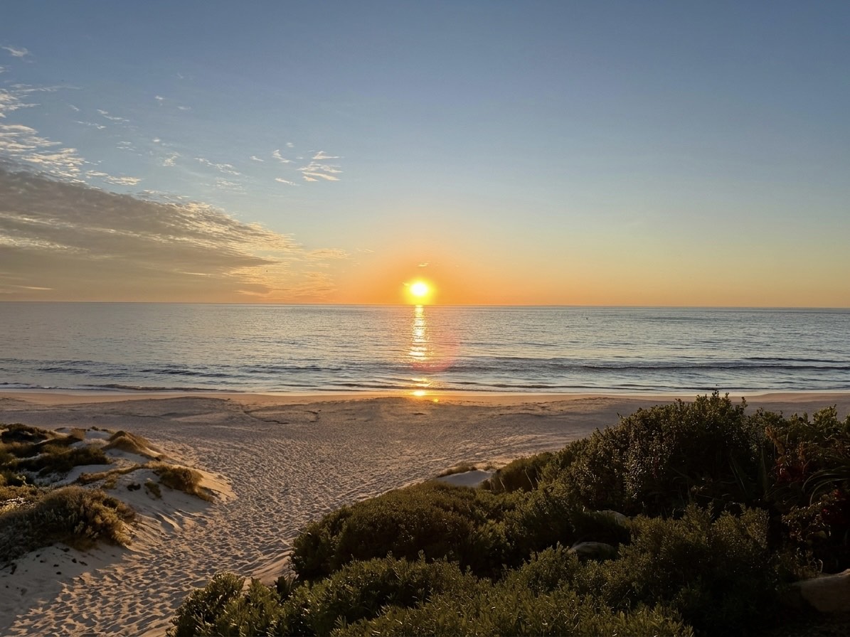 Beyond the dunes a calm sea opens to the horizon, the low sun laying a path of light across the water.